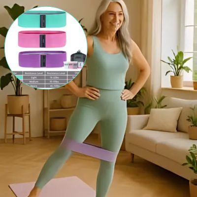 Femme de 50 ans dans son salon fait des exercices de renforcement des jambes avec l'élastique sport au-dessus des genoux avec une image loupe de trois élastiques sport différent vert, rose, violet différente force